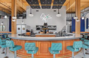 wide image of wood bar with blue barstools and a neon white sign of a chef on the wall