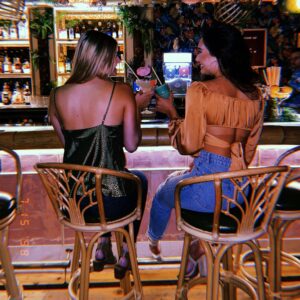 two young women sit at bar with cocktails