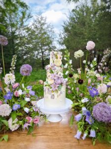 three-tiered floral, purple wedding cake surrounded by flowers